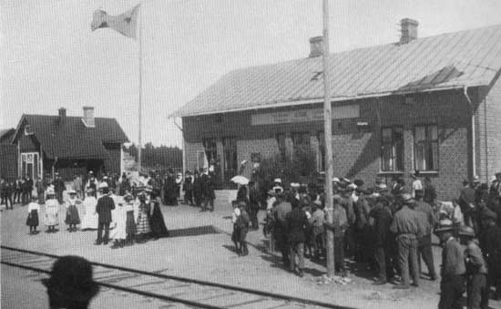 trans nya stationshus har flaggorna i topp med anledning av att hela WbJ ppnas fr allmn trafik 22 juli 1911. Fr att f ansluta sin jrnvg till stationen fick man betala fr ett nytt stationshus, godsmagasin, samt fr bangrdens utvidgning. Foto: Svenska Jrnvgsfreningens minnesskrift 1876-1926.